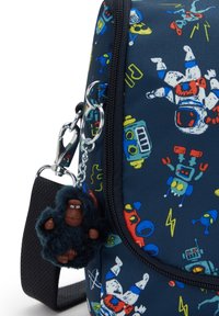La handbagi tummansininen, jossa on värikkäitä robotin ja astronautin kuvioita, ja siinä on pörröinen musta gorillan avaimenperä, joka on kiinnitetty metallikoukkuun.