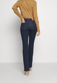 Mörkblå utsvängda jeans med hög midja, tillverkade av denim, med bakfickor och en brun läderlogga på midjebandet.