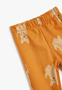 Oranssi legginsit, jotka on valmistettu pehmeästä kankaasta ja joissa on leikkisä karhukuosi koko pinnassa, sekä joustava vyötärö mukavuutta varten.