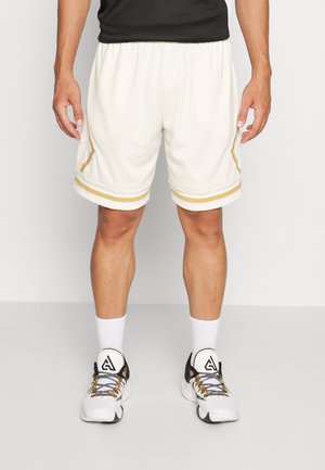 Mann trägt weiße Mesh-Basketballshorts mit goldenen Streifen, weiße Socken und weiße Sportschuhe mit schwarzen und goldenen Details.
