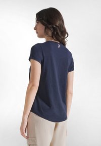 Granatowy t-shirt z krótkim rękawem, okrągłym dekoltem i małą metką z tyłu. Materiał wydaje się miękki i lekki.