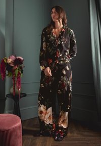 Černý květinový pyžamový set obsahuje velké bílé a červené květy, dlouhé rukávy, zapínání na knoflíky a široké kalhoty s odpovídajícími květinovými akcenty.