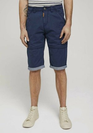 Marineblå bukser lavet af bomuld med opfoldet kant. Har forlommer og knaplukning, hvilket fremhæver et afslappet design.