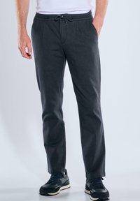 Dunkelgraue Jogginghose mit einem Kordelzugbund, schmal zulaufenden Beinen und seitlichen Taschen, aus einem weichen, strukturierten Stoff. Kombiniert mit schwarzen Sneakers.