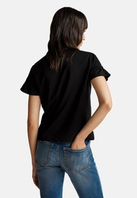 Camiseta negra de manga corta con un corte relajado y mangas con volantes, combinada con jeans de mezclilla azules que tienen bolsillos traseros y una textura desgastada.