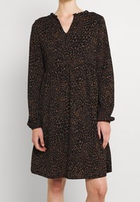 Svart klänning med brunt leopardmönster, v-ringning, långa ärmar och volangdetalj vid halsringningen. Lätt tyg med en lös passform.