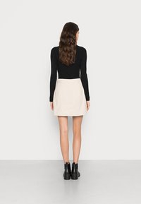 Haut �à manches longues noir, mini jupe beige et bottines noires. La jupe présente un design simple avec une texture subtile.