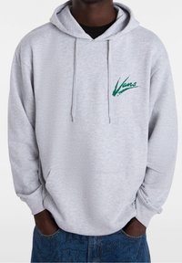Sudadera gris de algodón con un bolsillo tipo canguro en la parte delantera y capucha con cordón. Presenta un logo en verde de "Vans" en el lado izquierdo del pecho. Corte relajado.