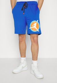 Shorts sportivi blu con texture a rete, cintura elastica con cordoncino e una grande grafica bianca e arancione sulla gamba sinistra.