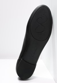 Semelle de chaussure plate noire avec talon texturé et grip à l'avant-pied, montrant la marque « Clarks » et une gravure en forme de cœur.