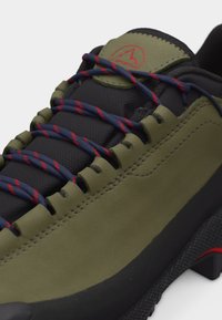 Πέδιλο πεζοπορίας σε ελιά και μαύρο χρώμα με κορδόνια σε σκούρο μπλε και κόκκινο, επενδυμένη γλώσσα και ανθεκτική υφή στην σόλα.