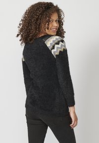Pull noir, duveteux, avec des manches longues et un dos texturé. Chevrons en gris, or et noir sur les accents d'épaules. Coupe classique.