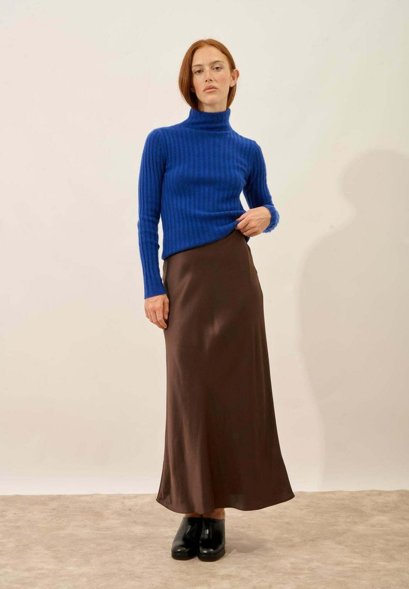 Blå ribturtleneck-tröja i kombination med en lång brun satinkjol. Modellen bär svarta platåskor. Neutral bakgrund.