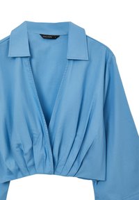 Camicia cropped blu chiaro con colletto, caratterizzata da una profonda scollatura a V e dettagli plissettati sul davanti. Realizzata in un tessuto morbido con una vestibilità morbida.