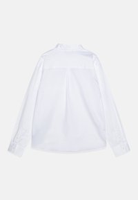 Bílá košile s dlouhými rukávy a límcem na knoflíky, detaily na zádech a akcenty na manžetách s knoflíky. Hladká textura a klasický design.