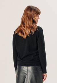 Zwarte wollen sweater met een gestructureerde afwerking, voorzien van een ronde halslijn en ribgebreide mouwen, gecombineerd met een hoogwaardige leren rok.