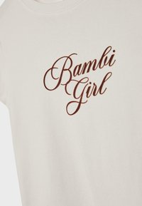 Cremefarbiges Baumwoll-T-Shirt mit kurzen Ärmeln, das auf der Vorderseite braune Schriftzüge mit "Bambi Girl" in einer kursiven Schriftart zeigt.