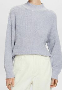 Lichtgrijze gebreide trui met een hoge hals, lange mouwen en geribbelde manchetten. Gecombineerd met lichtgekleurde broeken met een comfortabele pasvorm.