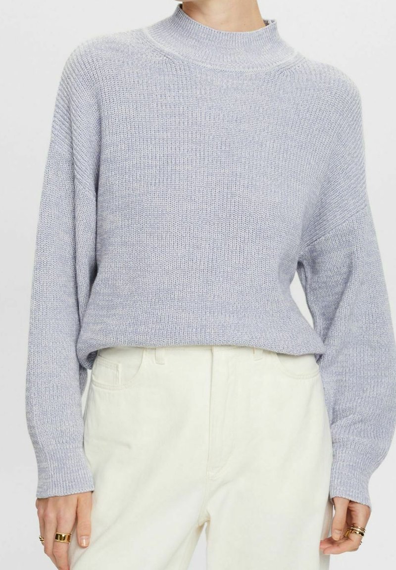 Lichtgrijze gebreide trui met een hoge hals, lange mouwen en geribbelde manchetten. Gecombineerd met lichtgekleurde broeken met een comfortabele pasvorm.