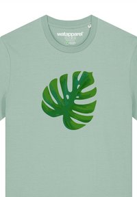 T-shirt vert clair avec un grand graphique de feuille de monstera de différentes nuances. Design à col rond avec des manches courtes.