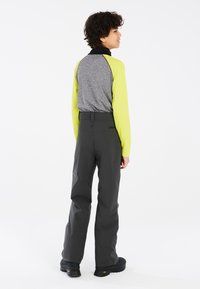 Maglietta a maniche lunghe grigia e lime con colletto nero, abbinata a pantaloni grigio scuro. Tessuto liscio; siluetta aderente, branding minimale sui pantaloni.