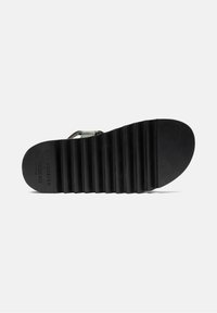 Czarna gumowa podeszwa sandała z wyraźną strukturą, z wyraźnymi liniami, tłoczonym logo oraz gładką, zaokrągloną częścią palców.