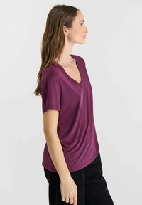 V-hals top met korte mouwen in diep paars, gemaakt van zachte stof met een relaxte pasvorm, met een vloeiende drape. Minimalistisch ontwerp, geen patronen.