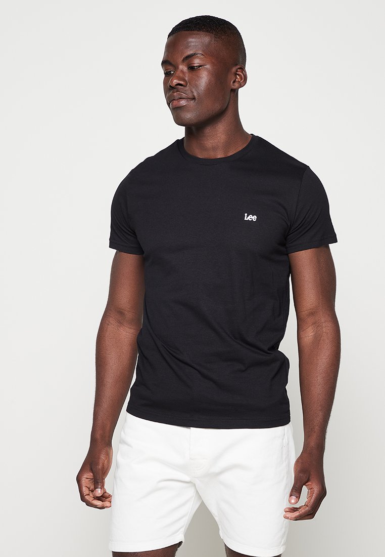 Czarny T-shirt krótki rękaw z bawełny, z małym białym logo "Lee" na lewej stronie klatki piersiowej. Gładka faktura. Model na zdjęciu nosi białe szorty.