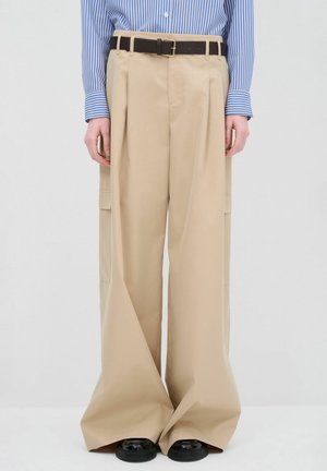 Pantalones de pierna ancha beige, confeccionados en una tela ligera, con bolsillos laterales, un cinturón negro y un acabado suave.