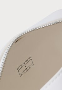 Scarpa bianca con un'esterno liscio, dotata di una cerniera argentata e di un logo stampato all'interno che riporta la scritta "TOMMY JEANS." Design semplice e minimalista.