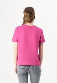 Tettsydd rosa bomull t-skjorte med rund hals og korte ermer; glatt tekstur; kombinert med falmet denim jeans med detaljerte baklommer.