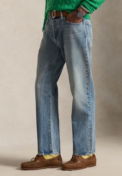 Άτομο που φοράει ανοιχτό μπλε τζιν με ίσια γραμμή, καφέ δερμάτινη ζώνη, καφέ μοκασίνια με κίτρινες κάλτσες και πράσινο πουλόβερ με πλέξη καλωδίου.