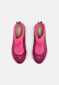 Zapatillas rosa sin cordones con parte superior brillante, panel elástico y un detalle en forma de corazón en la parte delantera. Suela de goma blanca.