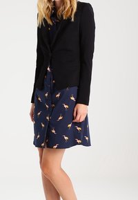 Musta kuvioitu bleiseri tummansinisen mekkoon, jossa on flamingokuvio. Bleiseri on vartaloa myötäilevä ja siinä on yksittäinen nappisulkeminen, joka korostaa asua.