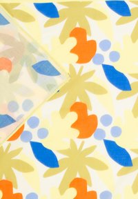 Tissu avec un motif floral abstrait coloré comportant des formes oranges, bleues, jaunes et vertes sur un fond blanc, plié dans un coin.