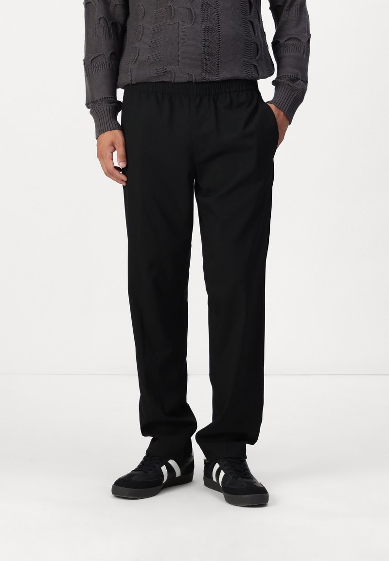 Svarta byxor med elastisk midja, raka ben och slät tyg. Kombineras med svarta sneakers med vita randiga detaljer.