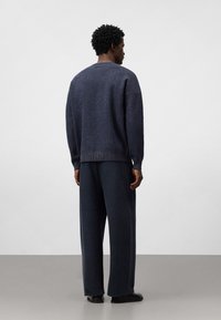 Marinblå stickad tröja med rund halsringning och ribbat fåll, parat med löst sittande marinblå byxor. Mjuk textur, minimalistisk design.