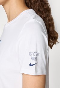 White cotton t-shirt featuring short sleeves, ribbed crew neck, and navy text on the sleeve reading "ICI C'EST PARIS" and Nike logo.