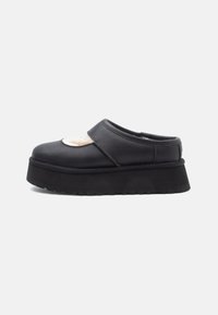 Sapatilha preta de plataforma slip-on com uma sola grossa e um topo recortado que revela um forro branco e macio no interior.
