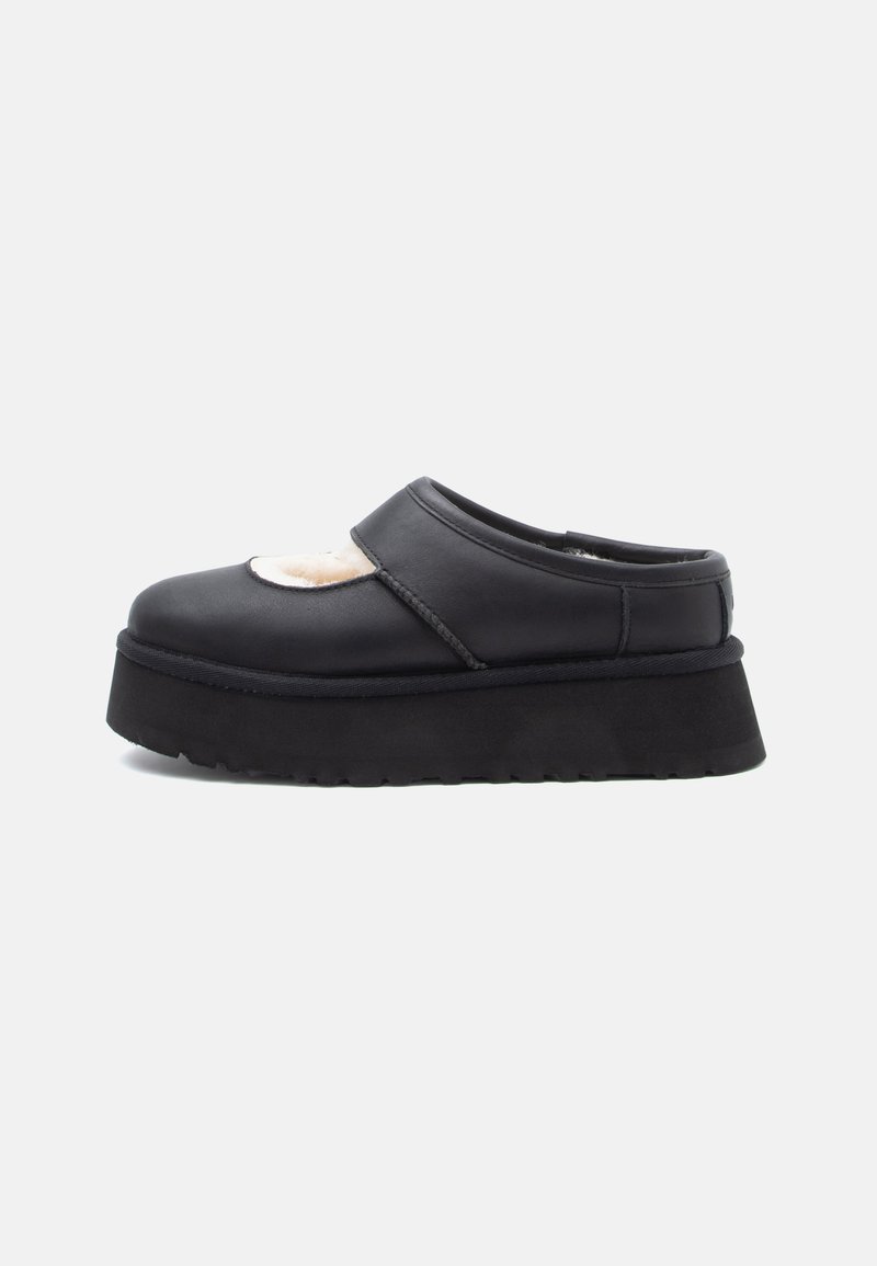 Sapatilha preta de plataforma slip-on com uma sola grossa e um topo recortado que revela um forro branco e macio no interior.