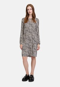 Langärmliges Kleid mit schwarzem Hintergrund und abstrakten cremefarbigen und rosafarbigen Mustern. Hat einen runden Halsausschnitt und einen lockeren Schnitt. Lederschuhe.