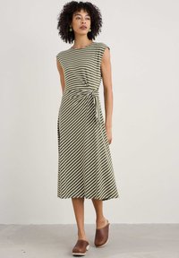 Gestreiftes Kleid in Olivgrün und Weiß, mit tailliertem Oberteil, Taillengürtel und knielangem Rock. Getragen mit braunen Holzclogs.