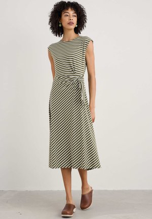 Striped dress in olive green and white, featuring a fitted bodice, waist tie, and knee-length skirt. Worn with brown wooden clogs.