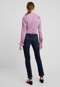 Ljuslila långärmad skjorta med rynkade ärmar, kombinerad med mörkblå skinny jeans med fickor och en medelhög midja.