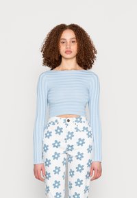 Top cropped de malha canelada azul claro com mangas longas, combinado com calças brancas com um padrão de flores azuis.