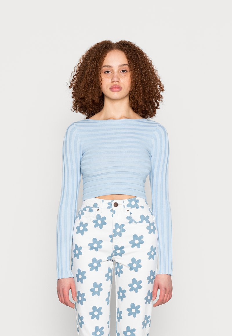 Top cropped de malha canelada azul claro com mangas longas, combinado com calças brancas com um padrão de flores azuis.