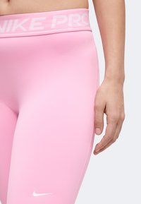Gros plan d'une personne portant des leggings Nike Pro roses avec un logo Nike blanc près de la cuisse et une ceinture portant l'étiquette "Nike Pro."
