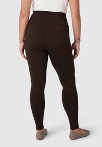 Leggings marroni con vita alta, realizzati in materiale elasticizzato, caratterizzati da una texture liscia e un design aderente.