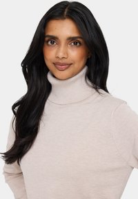 Ljusbeige polotröja i mjukt ribbat stickat tyg, med en åtsittande design och långa ärmar.