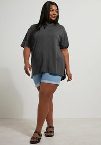 Dark gray oversized t-shirt with short sleeves, paired with light blue denim shorts. Black strappy sandals complete the look.